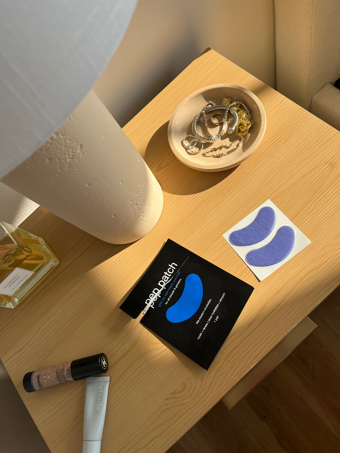 Pep Patch eye patches and black sachet arranged on a sunlit bedside table with morning essentials